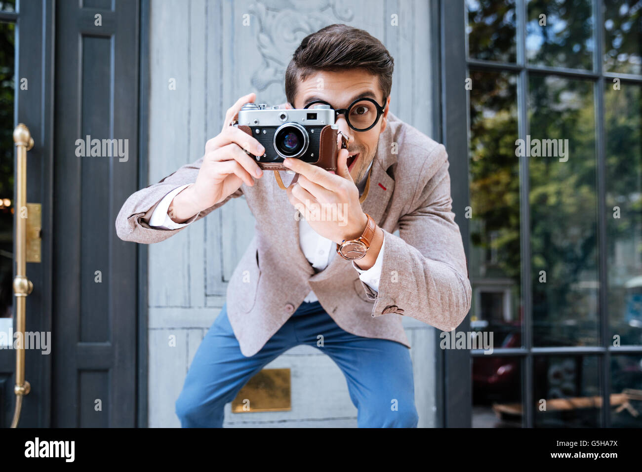 Smiling funny photographe en lunettes rondes à l'aide d'ancien appareil photo et prendre des photos en plein air Banque D'Images