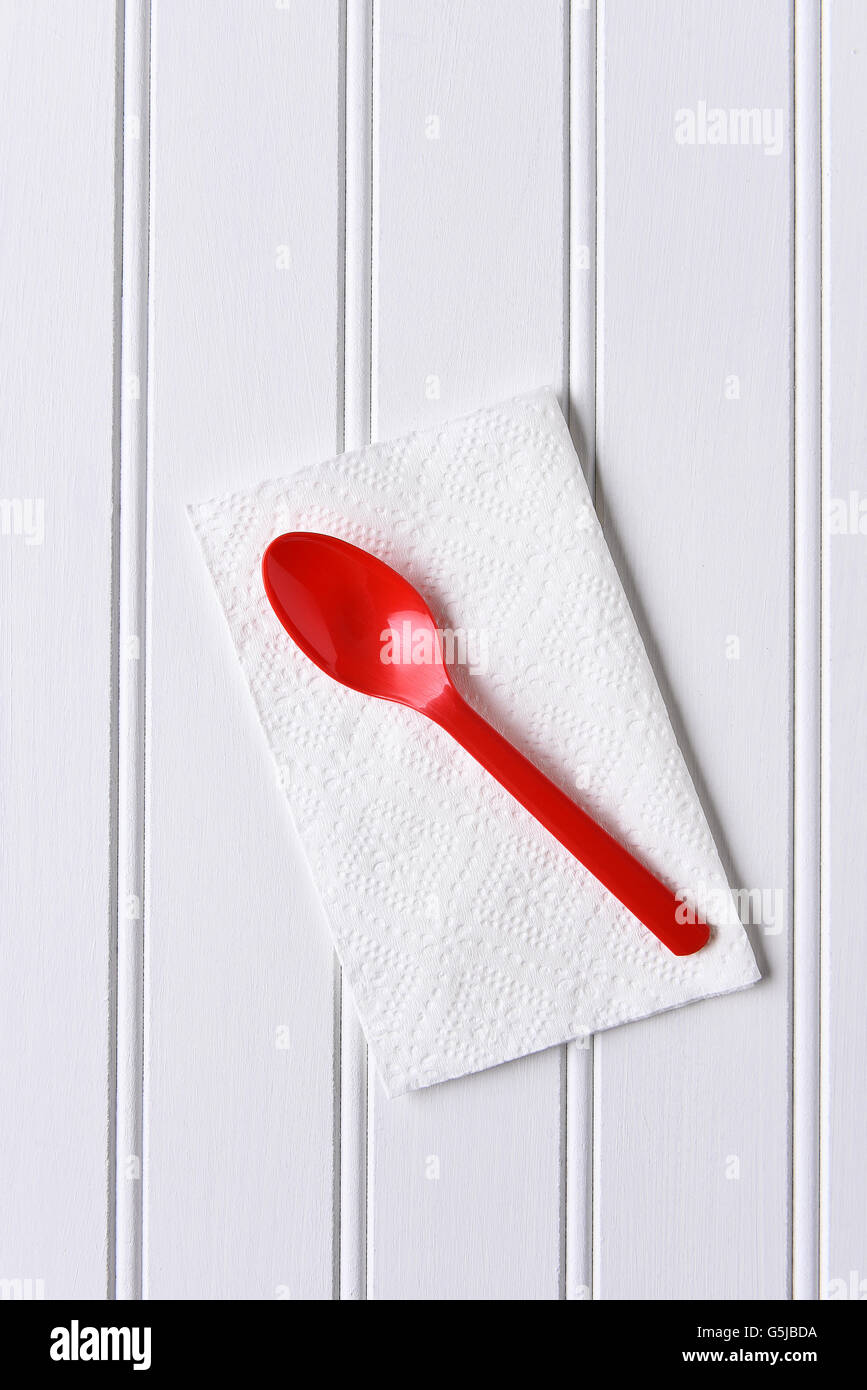 Vue de dessus d'une cuillère en plastique rouge sur une serviette blanche sur un tableau blanc. Format vertical avec copie espace. Banque D'Images