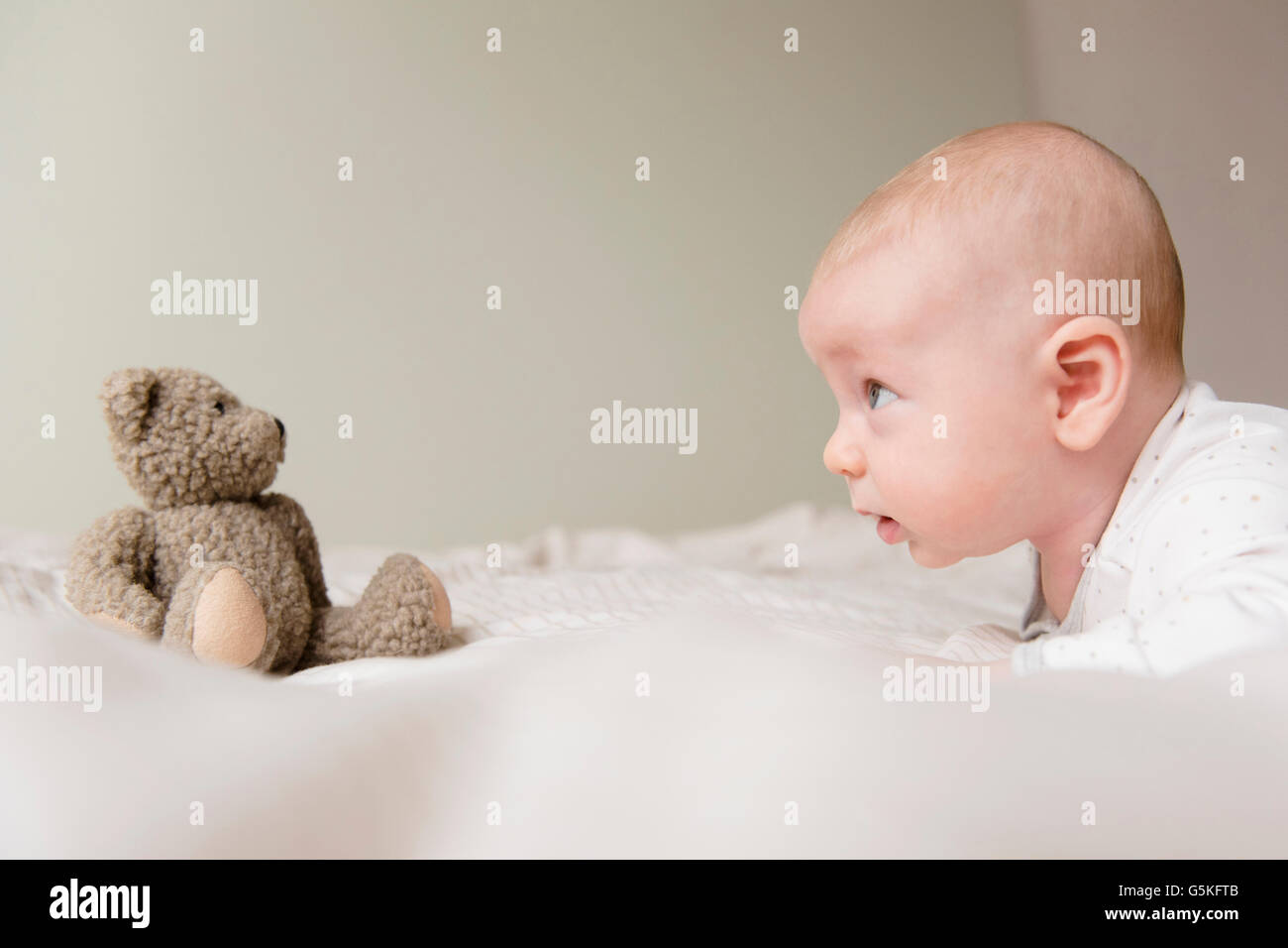 Caucasian baby regardant teddy bear on bed Banque D'Images