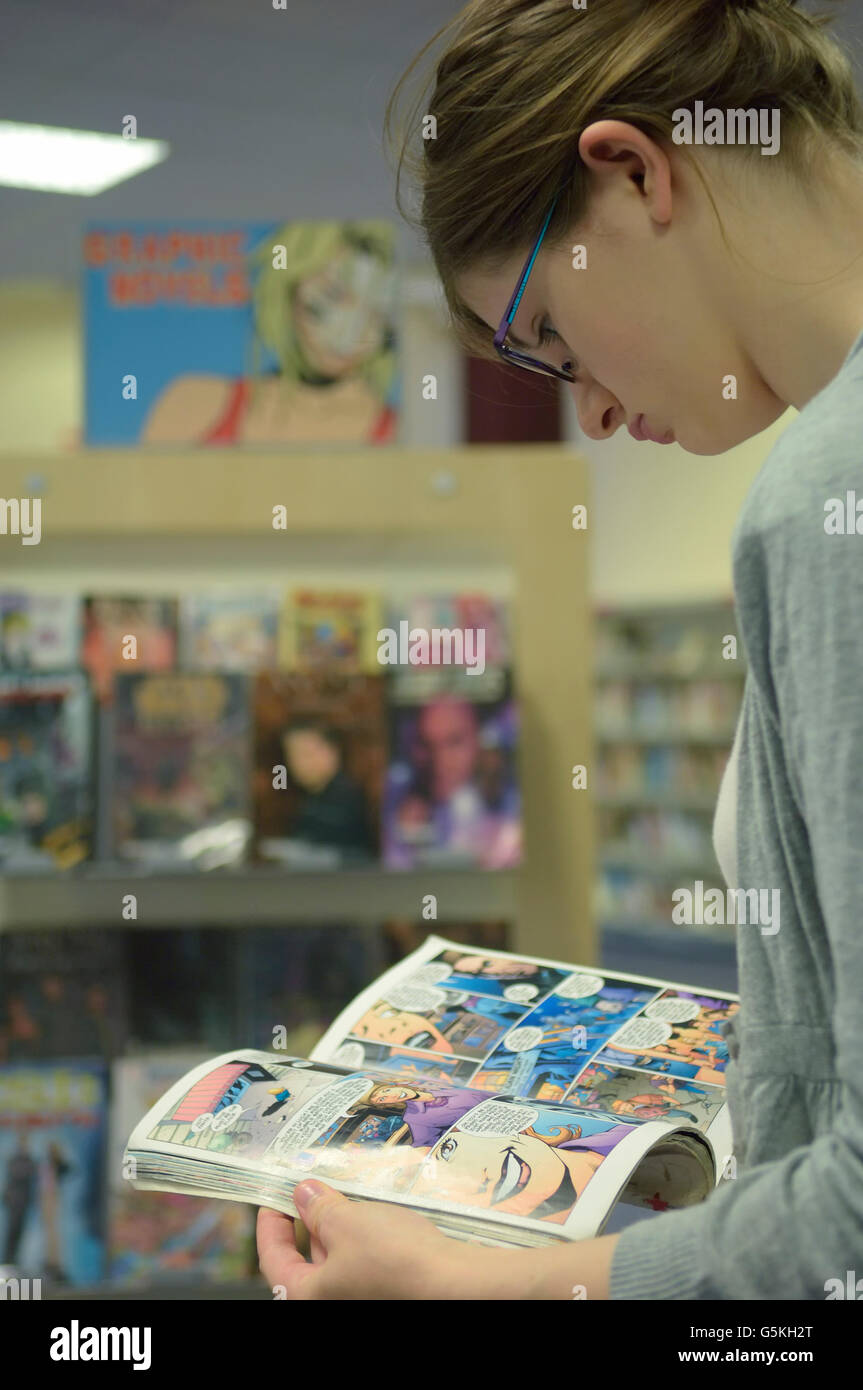 Une jeune femme lisant un roman graphique dans une bibliothèque publique. L'Angleterre. UK Banque D'Images