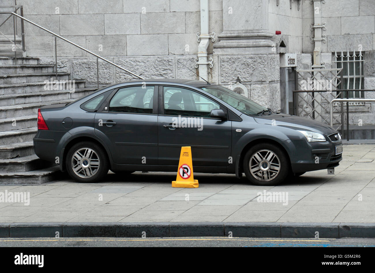 Une voiture garée sur le trottoir à côté d'un 'No Parking jaune bight' traffic cone, ville de Cork, County Cork, Irlande (Eire). Banque D'Images
