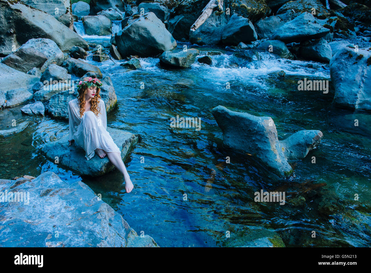 Caucasian woman wearing flower crown on rock at river Banque D'Images