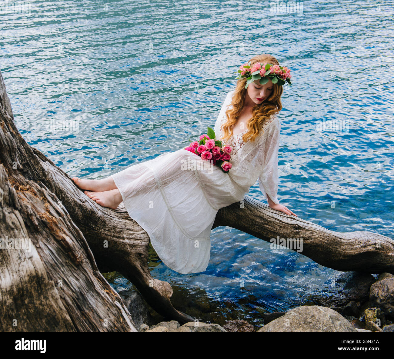 Caucasian woman wearing flower crown on log at river Banque D'Images