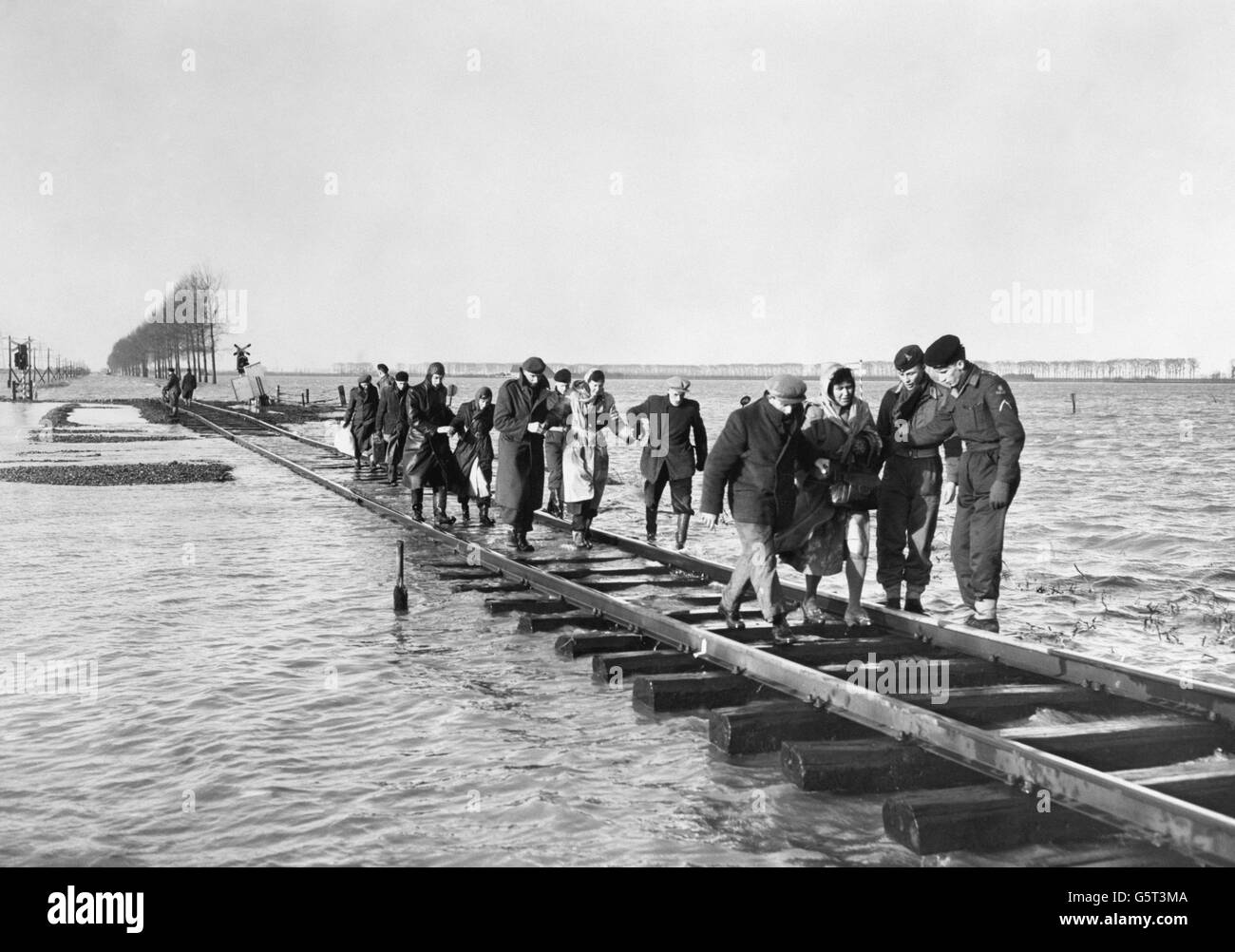 Les soldats aident à secourir les gens de leurs foyers en Zélande, province du sud-ouest de la Hollande, sur la mer du Nord, en utilisant une voie ferrée comme pont sur une vaste étendue d'eau d'inondation en route vers un lieu de sécurité. Banque D'Images