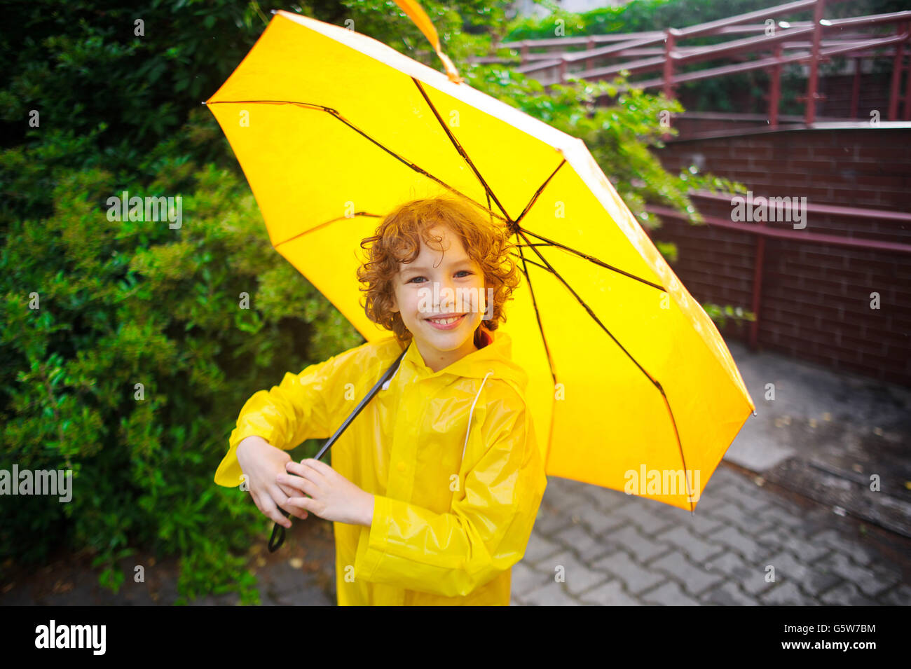 Le gentil Garçon de 8-9 ans sous un parapluie jaune. Le garçon dans un  imperméable jaune lumineux est titulaire d'un grand parapluie en main. Les  enfants Photo Stock - Alamy