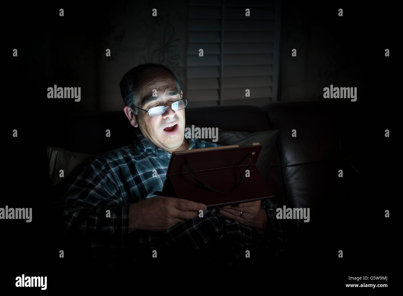 Le bâillement middle aged man wearing pajamas Tablette de lecture la nuit au lit avec copie espace Banque D'Images