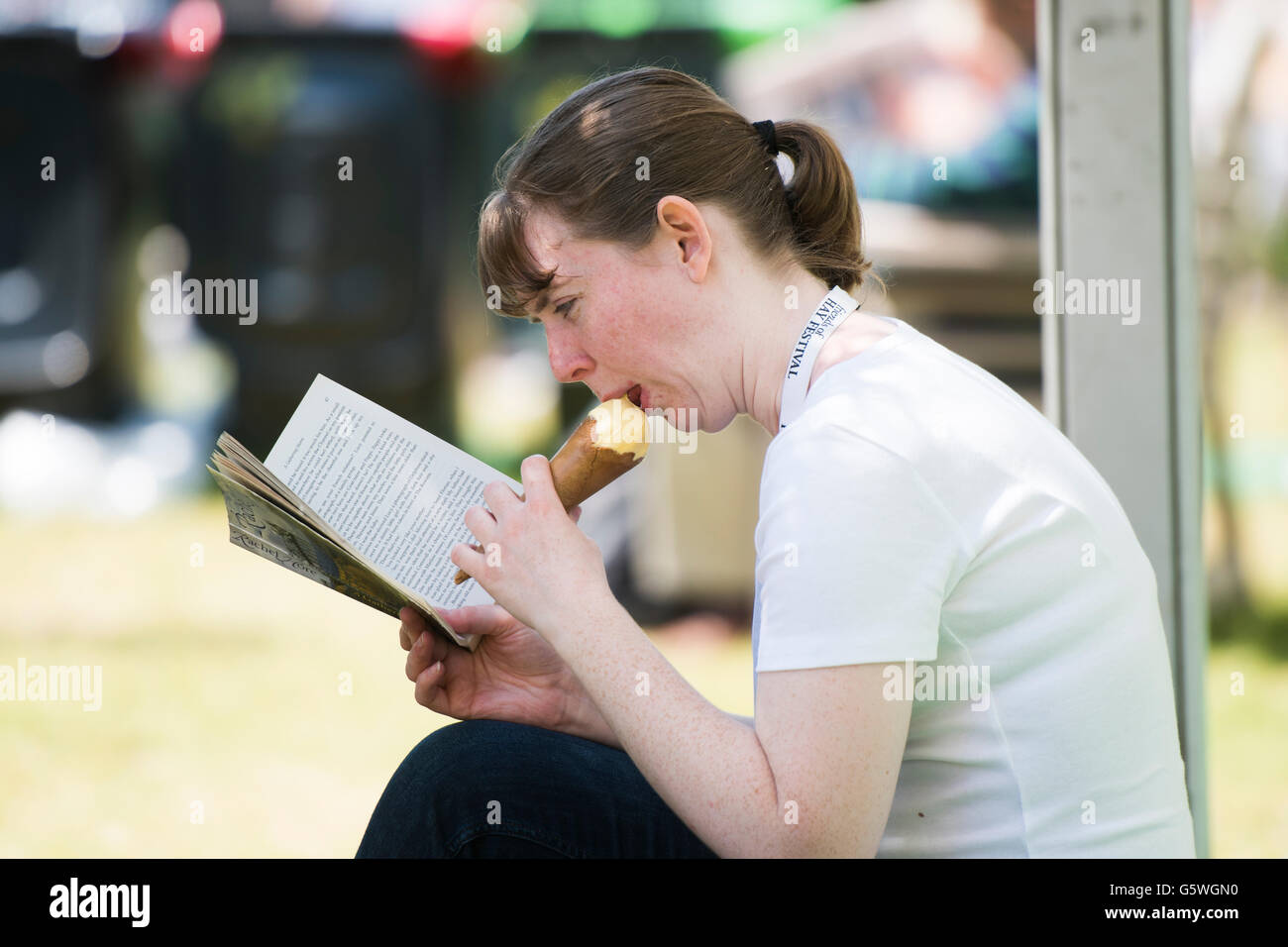 Bénéficiant d'une jeune femme qui mange une glace et la lecture d'un livre dans le chaud soleil d'été au Hay Festival de la littérature et les arts, Hay-on-Wye, Powys, Pays de Galles, Royaume-Uni, Dimanche 05 Juin 2016 Banque D'Images