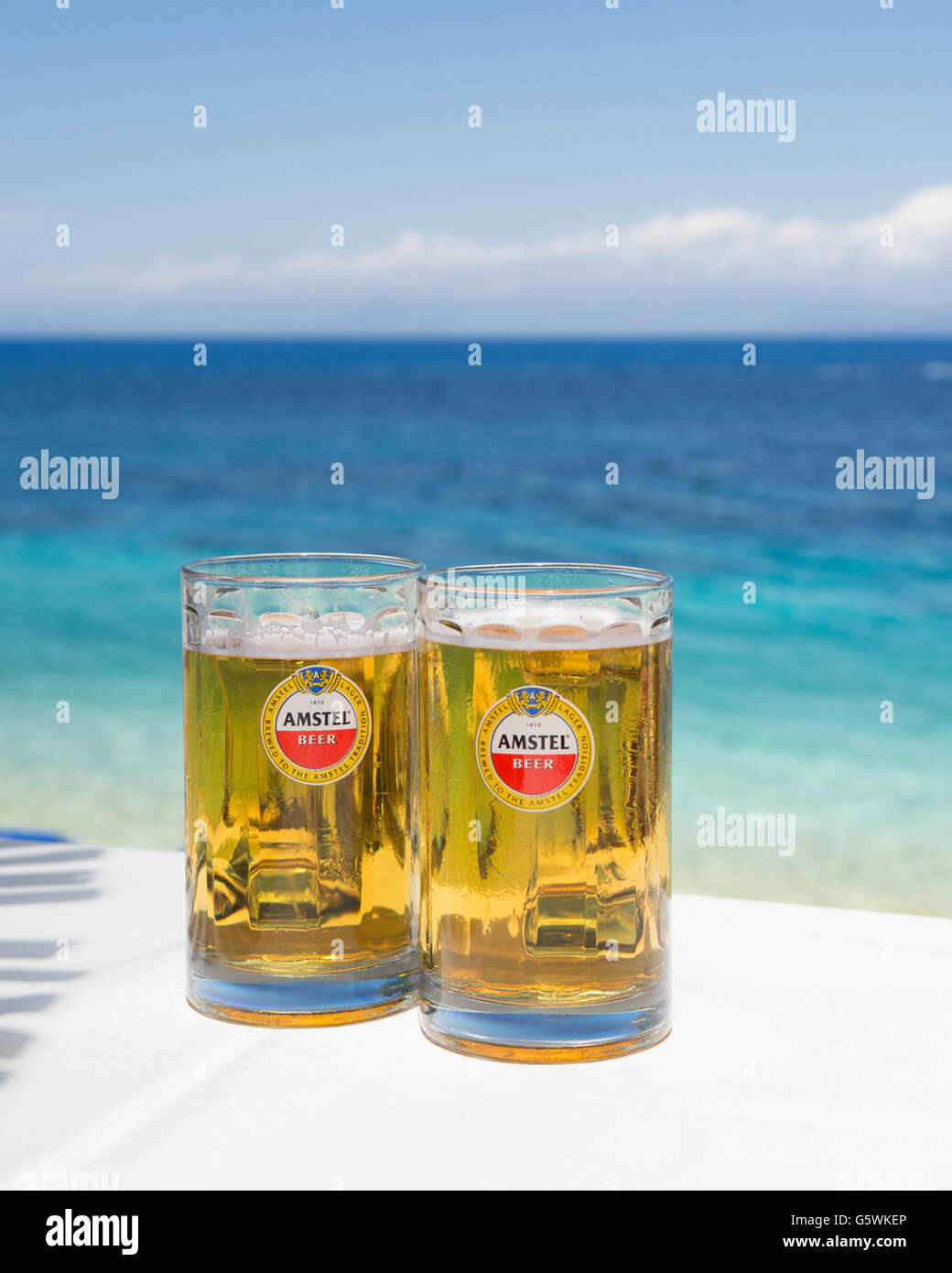 Pinte de bière Amstel glasses on white table au bar de plage avec mer en arrière-plan Banque D'Images