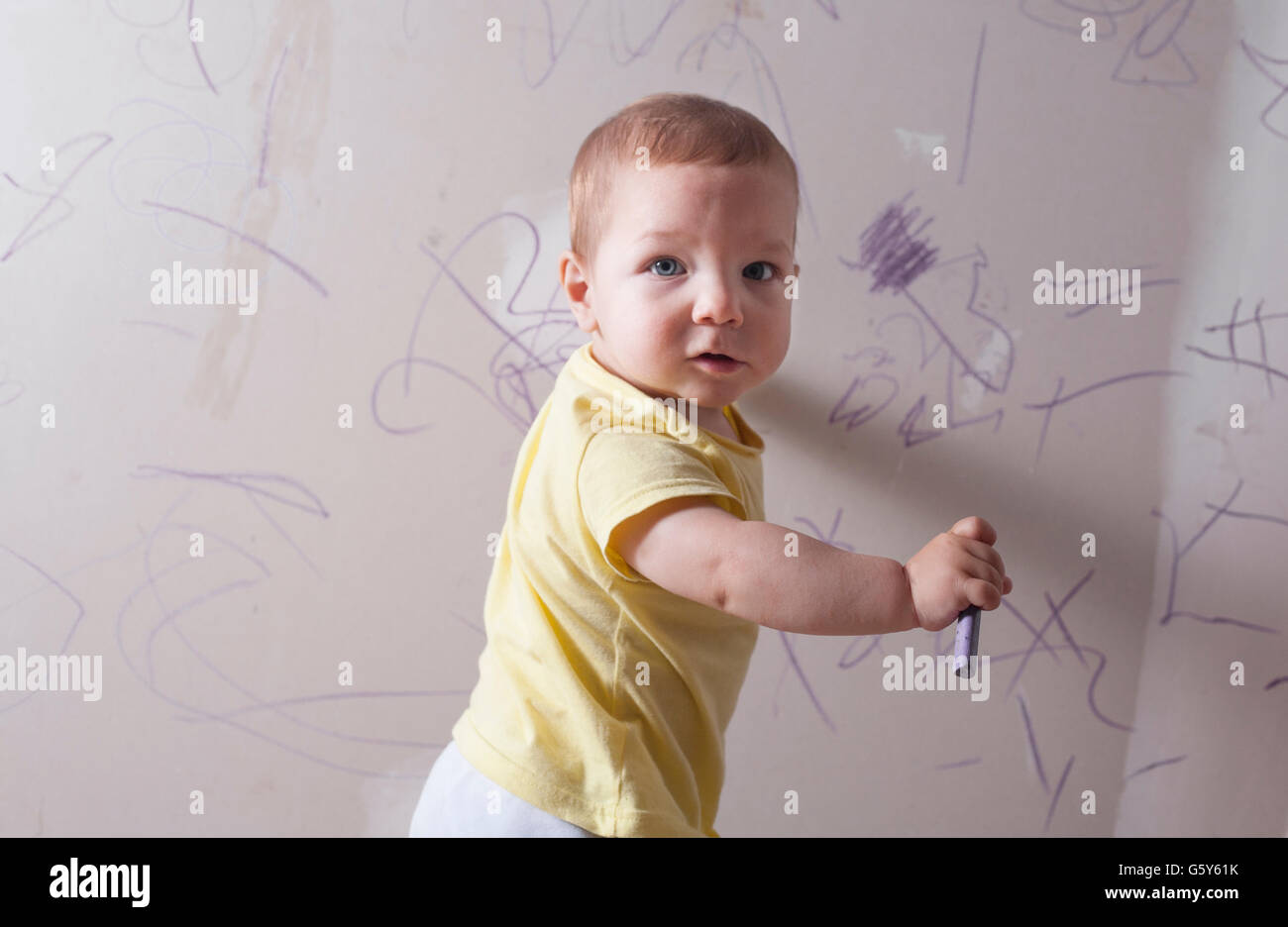 Baby Boy dessin avec crayon de cire sur le mur de plâtre. Il est à la recherche de l'appareil photo Banque D'Images