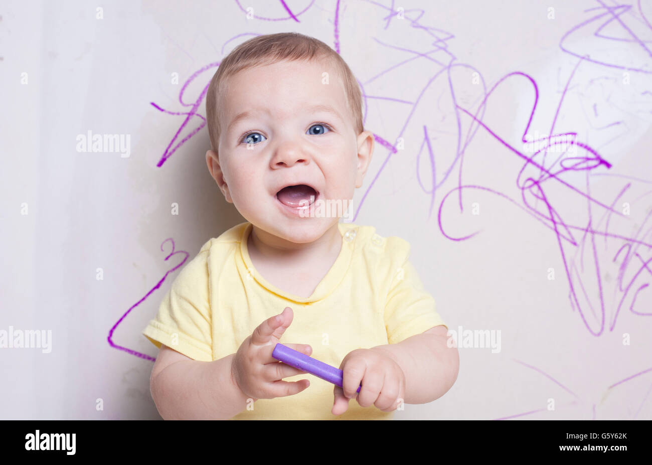Baby Boy avec crayon de cire sur le mur de plâtre. Il est à la recherche de l'appareil photo Banque D'Images