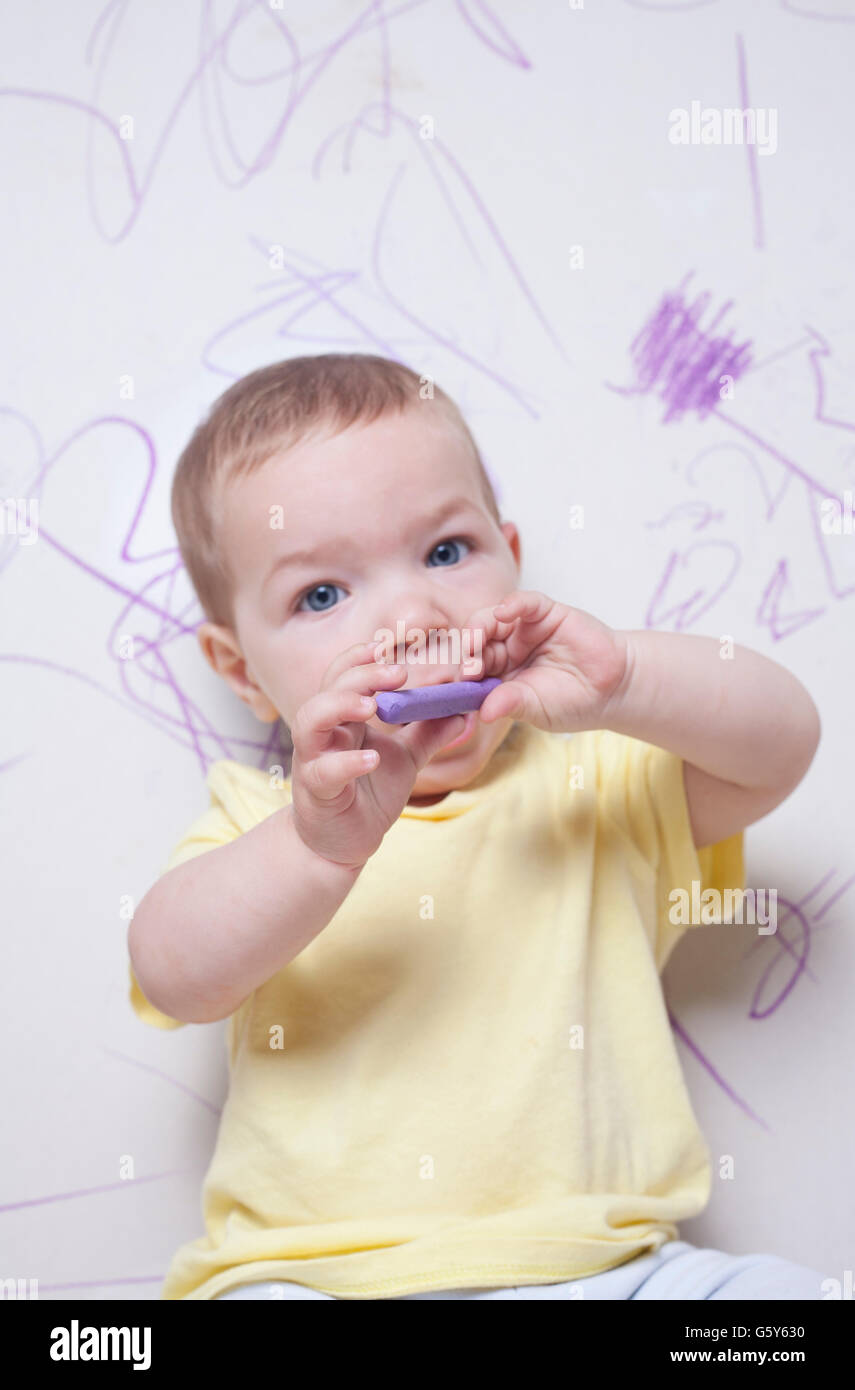 Baby Boy avec crayon de cire sur le mur de plâtre. Il est à la recherche de l'appareil photo Banque D'Images
