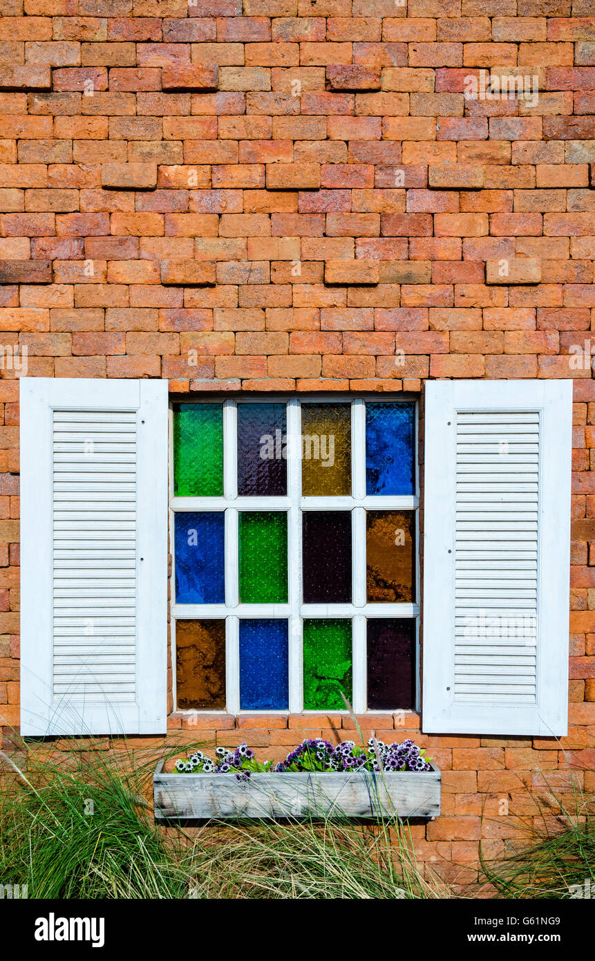 Fenêtre en verre blanc et coloré sur le mur de brique orange Banque D'Images