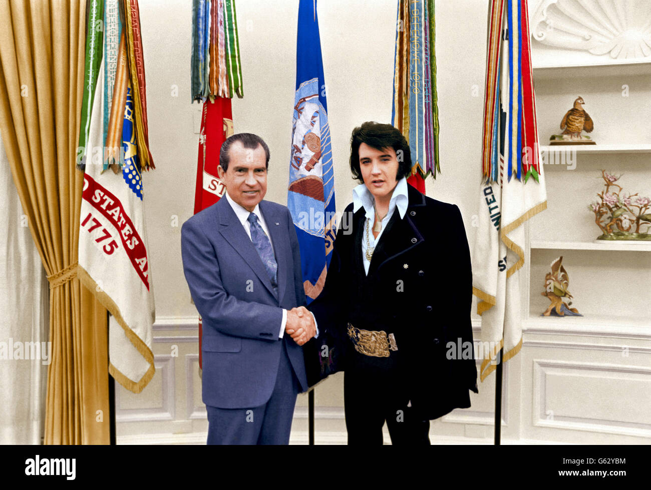 Elvis Presley, serre la main du président américain Richard M. Nixon en tant que membre du personnel de la Maison Blanche Egil Krogh regarde sur dans le bureau ovale à la Maison Blanche le 21 décembre 1970 à Washington, DC. (Note au rédacteur : l'image original est en noir & blanc et a été colorisée artificiellement pour simuler une authentique image couleur. Rien d'autre n'a été changé ou modifié.) Banque D'Images