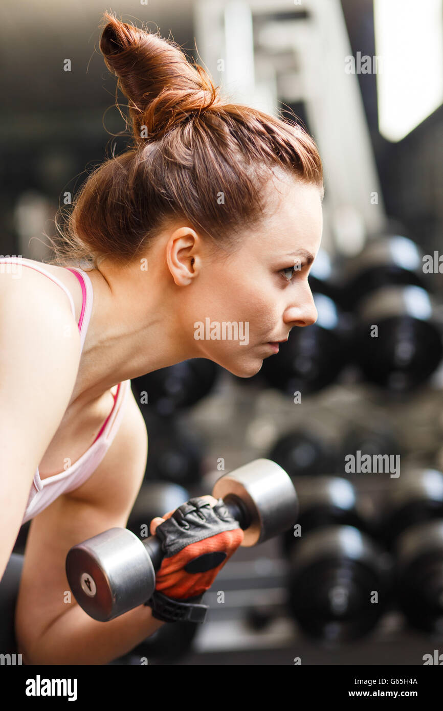 Jeune femme confiante biceps faisant de l'exercice avec haltères en centre de remise en forme. Formation fille Slim dans le sport avec haltères Banque D'Images