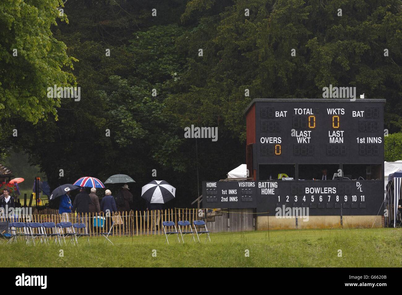 Les fans de cricket sous parasols passent le tableau blanc du Arundel Cricket Club, West Sussex où la pluie a retardé le début du LV= County Championship Division One match entre Sussex et Surrey. Banque D'Images