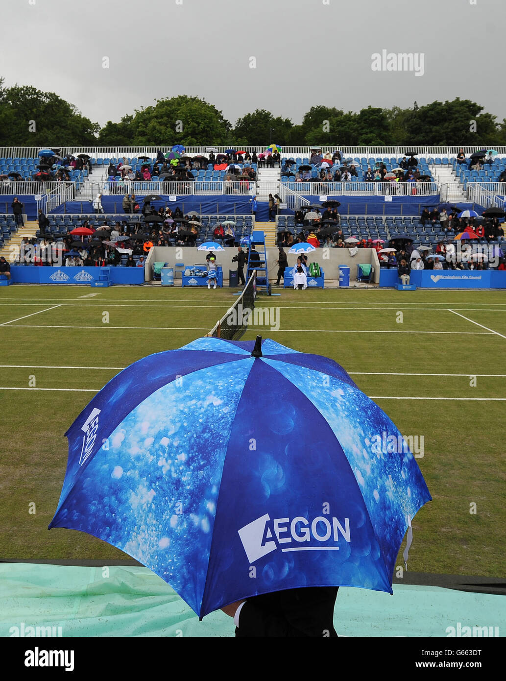 Les spectateurs prennent la couverture sous les parasols alors que le  personnel de terrain se prépare à apporter les couvertures sur le court  central avant tout jeu dans la demi-finale entre Magdelana