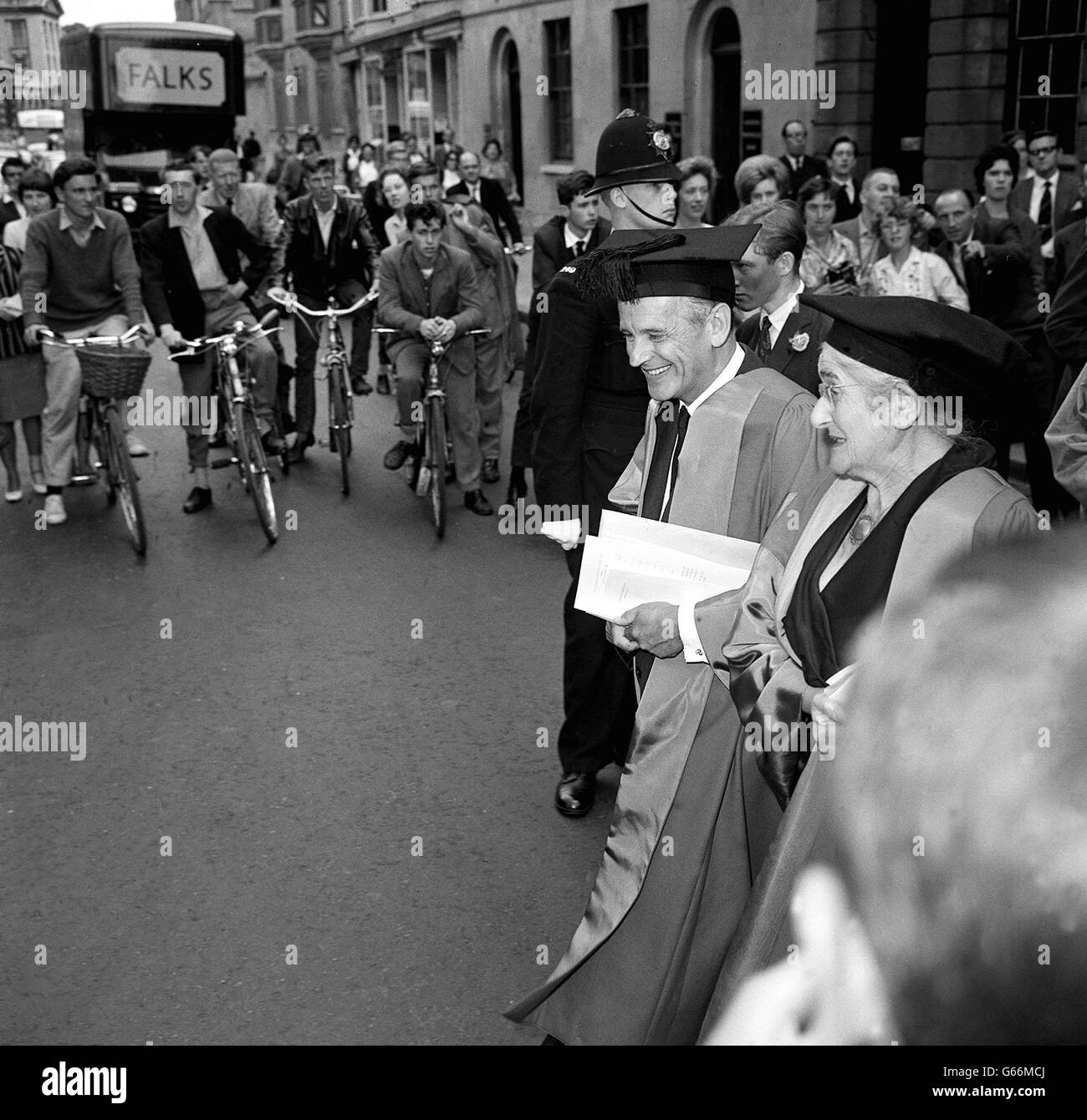 Les cyclistes s'arrêtent et les gens sur les trottoirs occupés font une pause pour observer les récipiendaires des diplômes honorifiques de l'Université d'Oxford quitter l'hôtel de ville d'Oxford, après l'Encaenia.Les honneteux souriants sont Graham Sutherland, le peintre, et Helen Maud Cam, l'historien médiéval, qui a tous deux reçu le titre honorifique de docteur en lettres. Banque D'Images