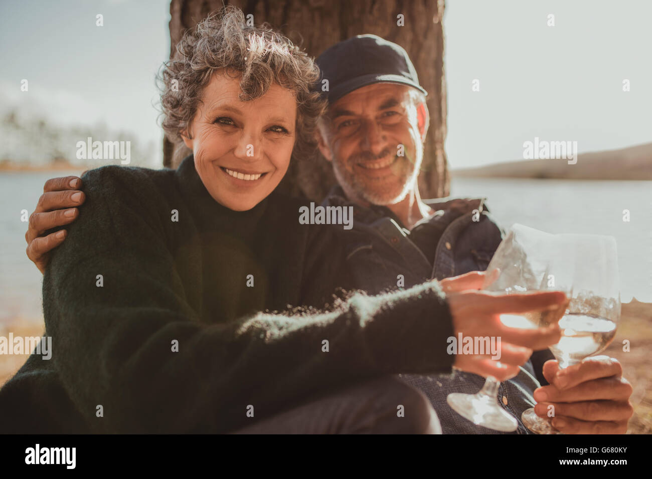Portrait of smiling mature couple assis avec un verre de vin. L'homme et la femme camping près d'un lac un jour d'été. Banque D'Images