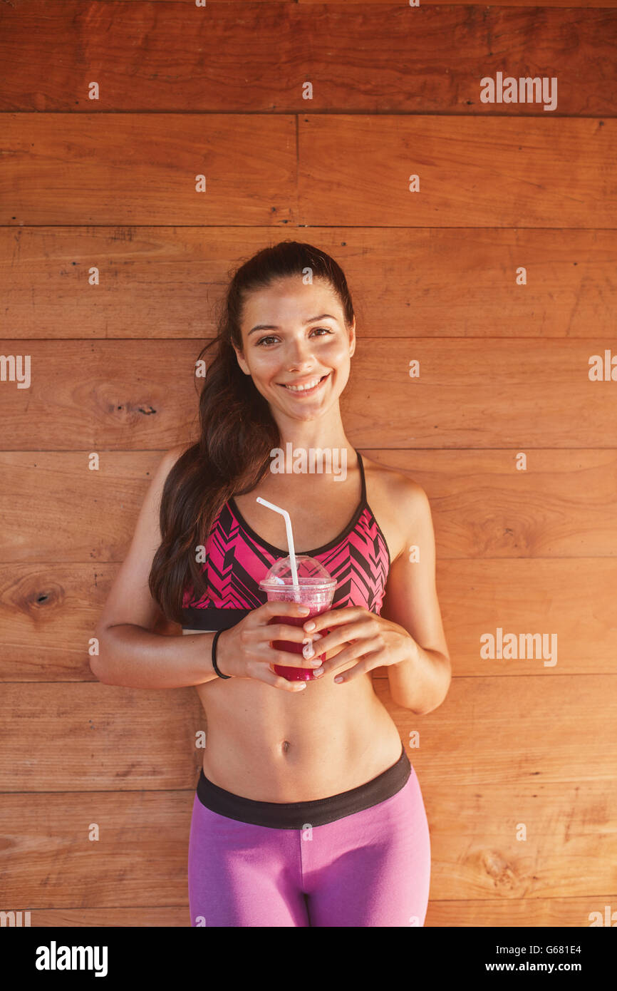 Portrait de jeune femme souriante avec verre de jus de fruit sur fond de bois. femme de fitness en vêtements de sport avec jus après Banque D'Images