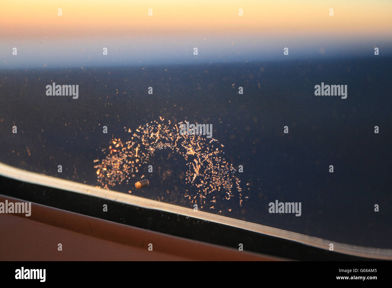 Un anneau de cristaux de glace se forment autour d'un petit trou dans la fenêtre d'un avion, avec un lever de soleil en arrière-plan. Banque D'Images