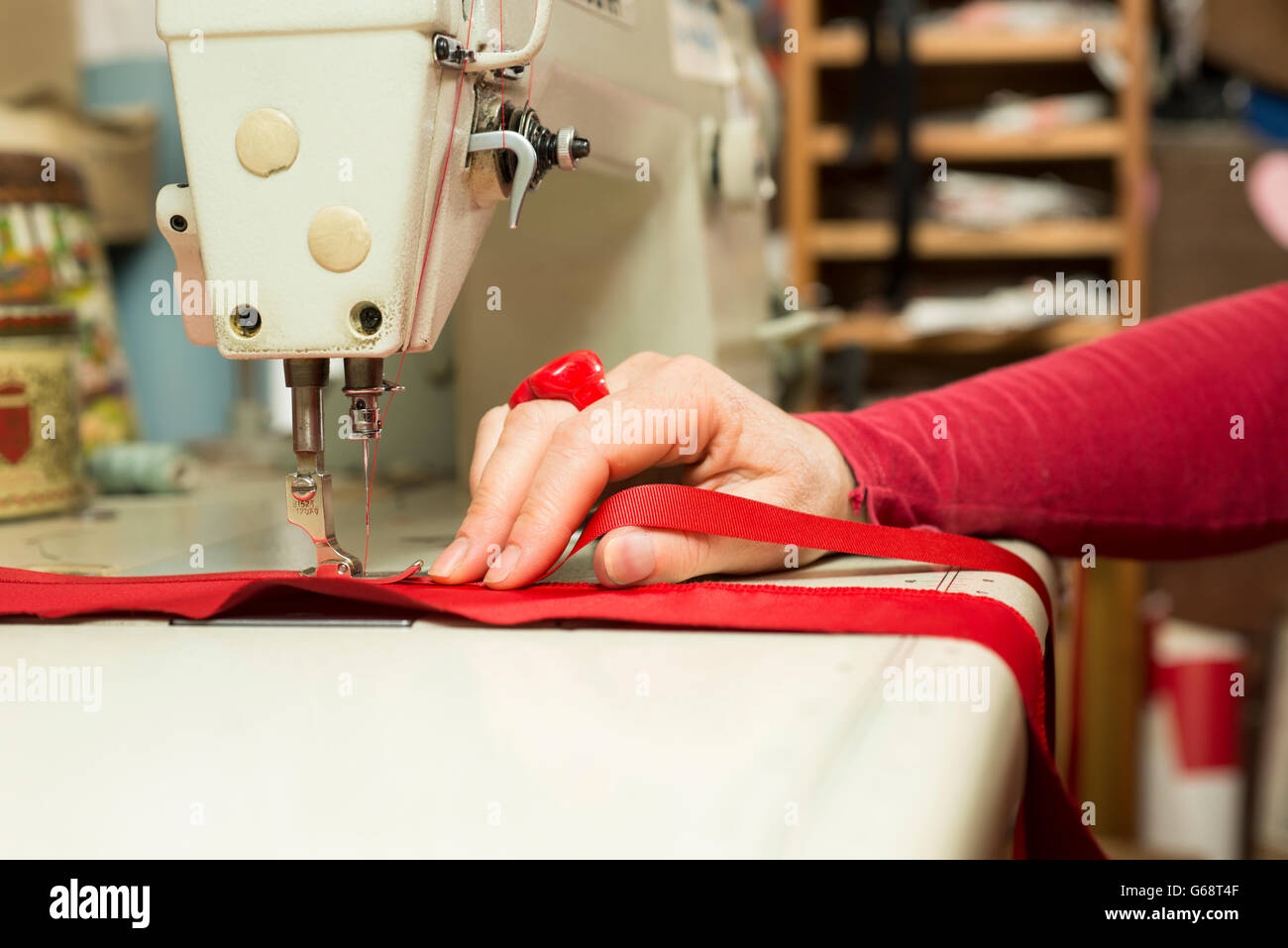 Main couturière soutenant un morceau de tissu rouge étant fixé au ruban satin par une machine à coudre Banque D'Images