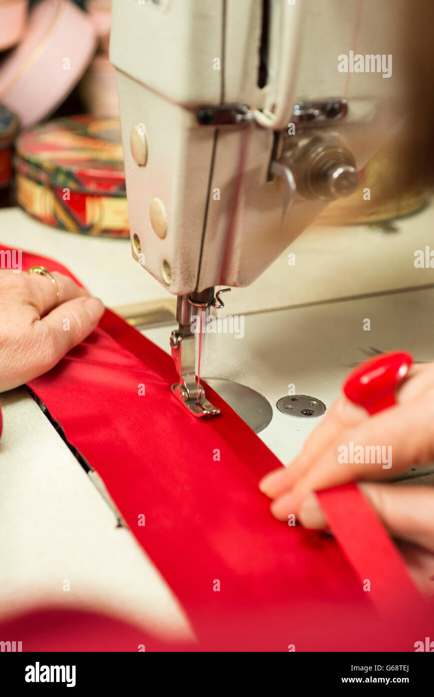 Les mains du tailleur soutenant un morceau de tissu rouge étant fixé au  ruban satin grâce à une machine à coudre Photo Stock - Alamy