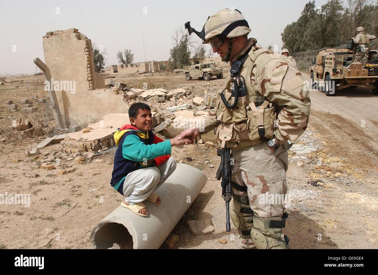 Un soldat américain secoue la main avec un curieux garçon irakien à la frontière avec le Koweït alors qu'ils observent l'arrivée de l'un des premiers transferts d'eau, vers la ville portuaire d'Umm Qasr, dans le sud de l'Irak.* le premier convoi de secours d'une taille importante s'est enroulé en Irak au milieu d'une tempête de sable alors que les forces américaines et britanniques ont lutté pour dégager la voie pour plus d'expéditions d'aide. Banque D'Images
