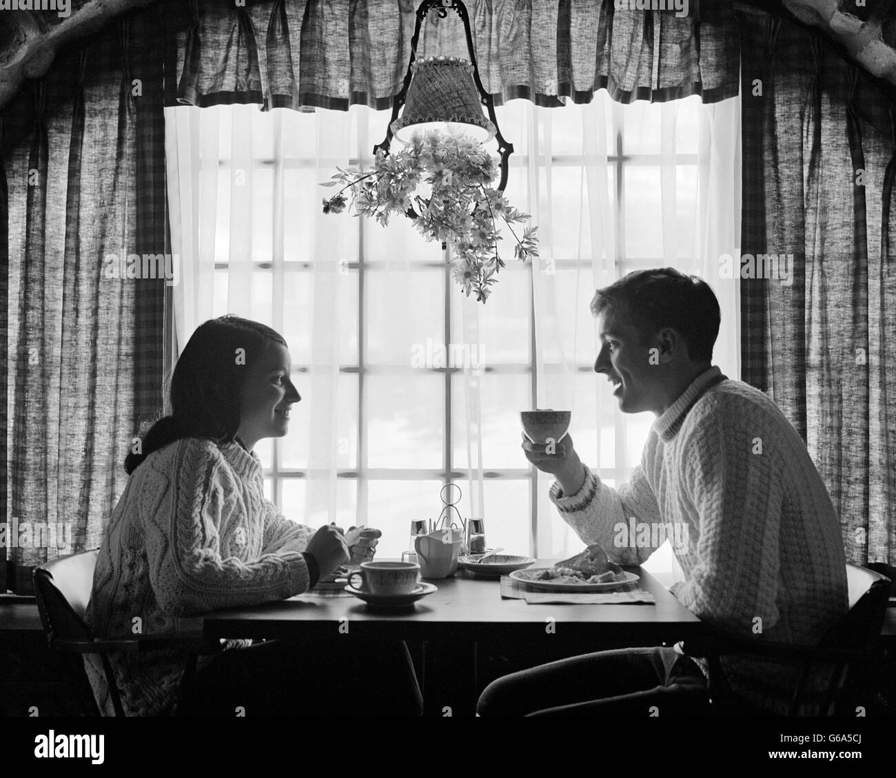 Des années 1970, la silhouette du couple EATING BREAKFAST À TABLE PAR FENÊTRE Banque D'Images