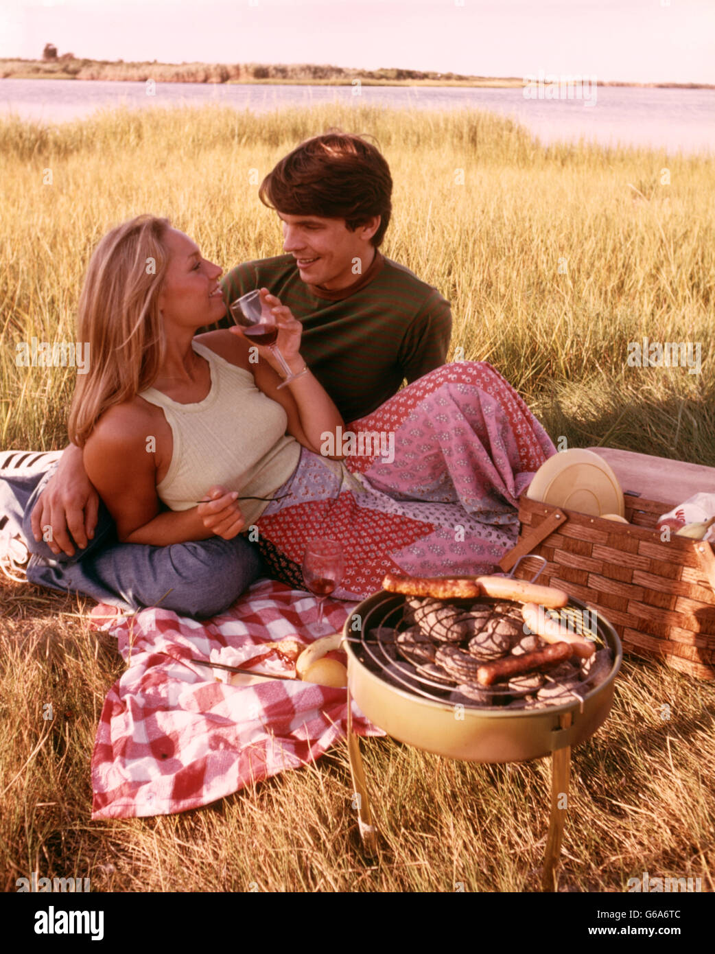 1970 Pique-nique dans l'HERBE JEUNE COUPLE DRINKING WINE hot-dogs sur le gril Banque D'Images