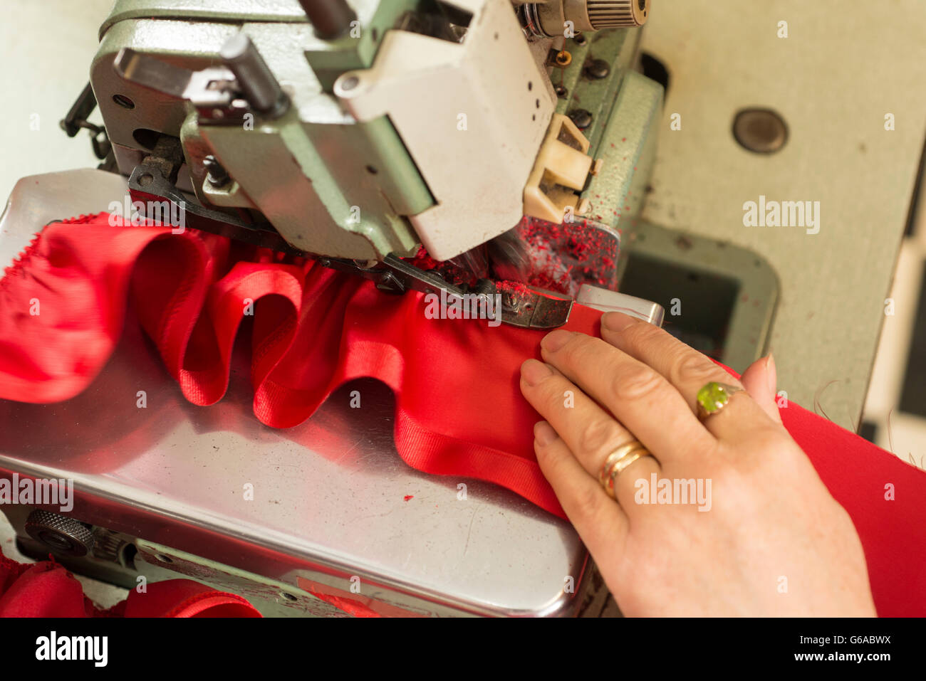 La main d'un tailleur soutenant un morceau de tissu froissé d'être dans une machine à coudre Banque D'Images