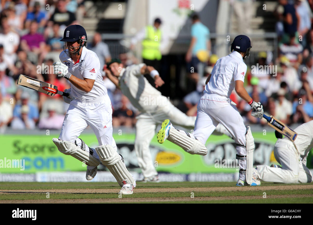 Le batteur d'Angleterre Alastair Cook et Joe Root courent entre le cricket, tandis que les trys Shane Watson d'Australie courtiont Cook Out avec jeter à des souches au cours du deuxième jour du troisième match d'essai de cendres d'Investec au terrain de cricket d'Old Trafford, à Manchester. Banque D'Images