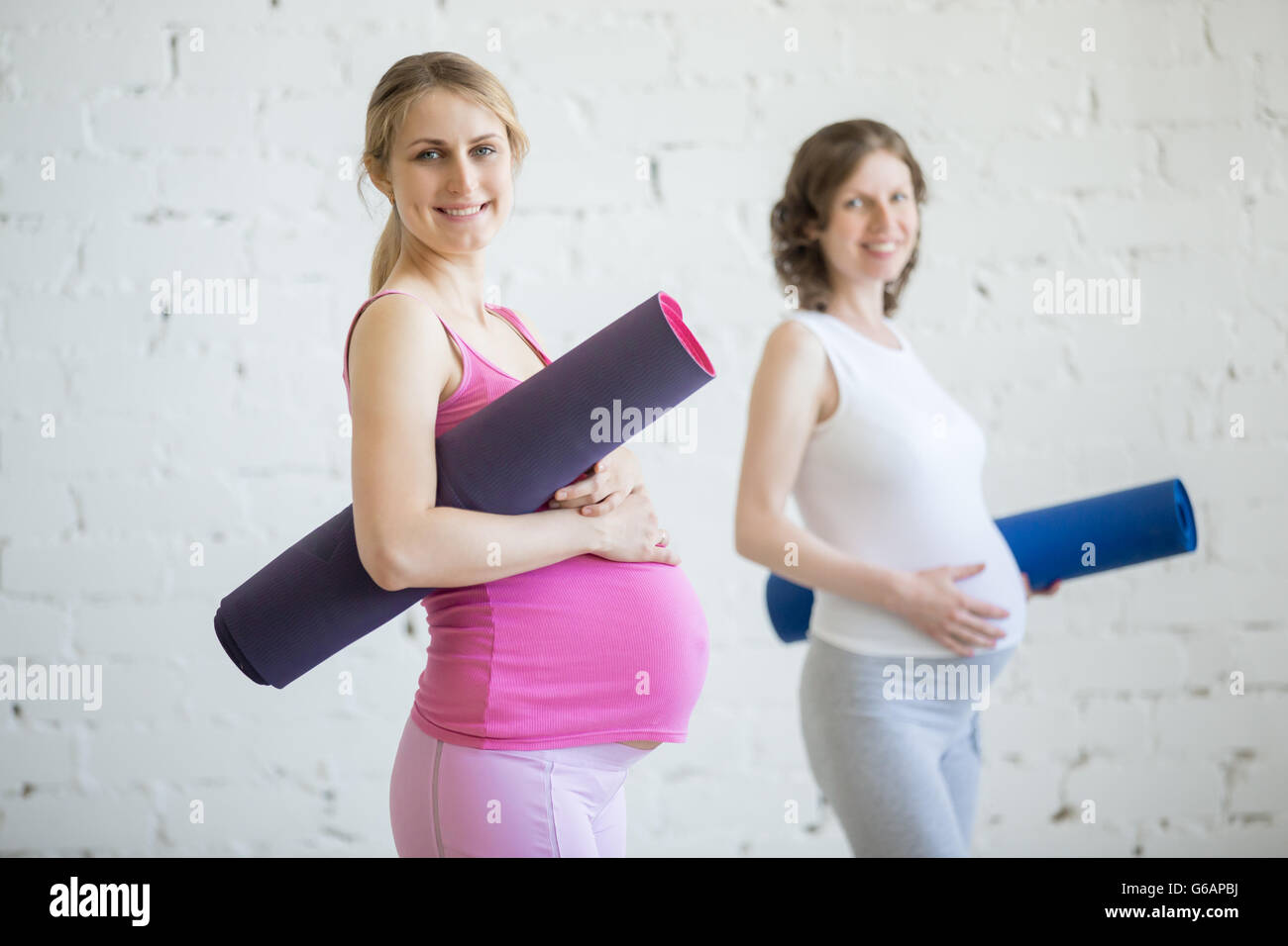 La grossesse Yoga, concept de remise en forme. Portrait de deux jeunes femmes enceintes yoga des modèles posant avec tapis de sport contre mur blanc Banque D'Images