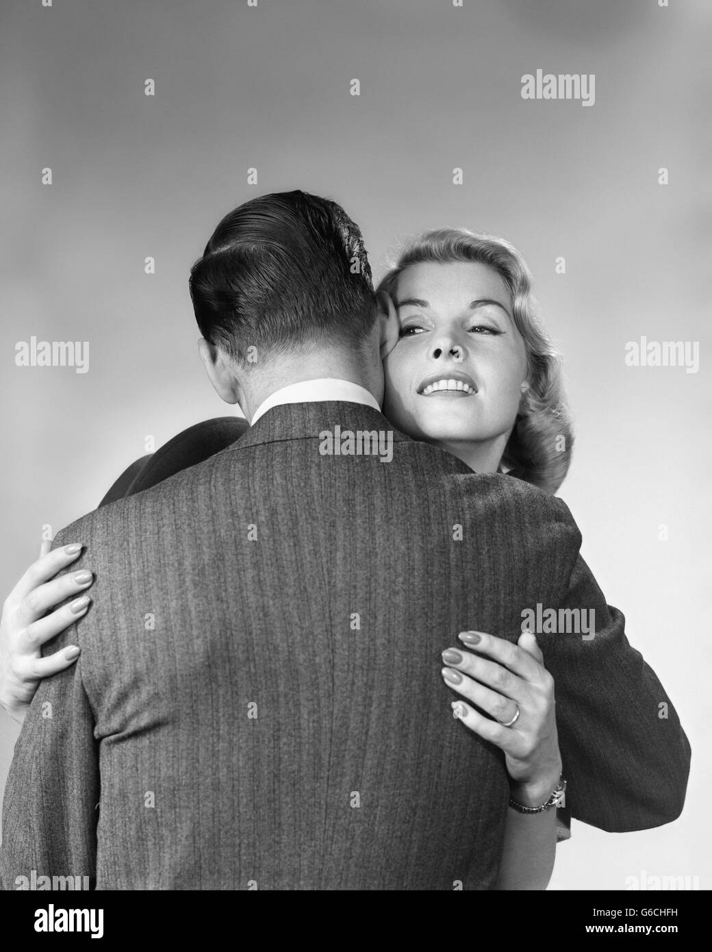 Années 1950 Années 1960 WOMAN HUGGING MAN AVEC SON DOS À L'APPAREIL PHOTO Banque D'Images