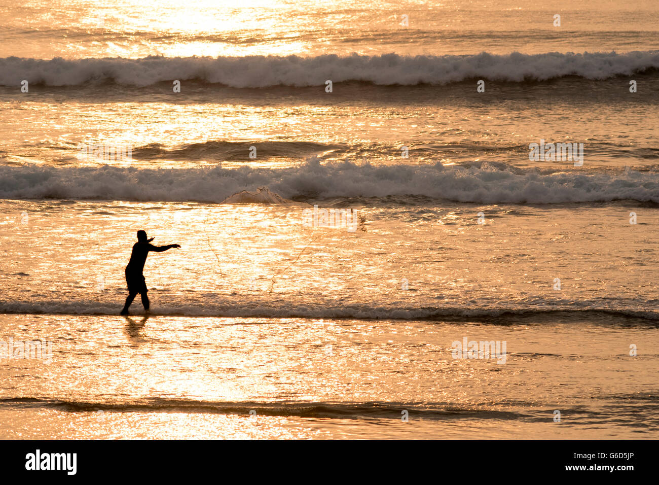Filet de pêche pêcheur jetant sur plage côte d'été, scène calme à l'heure du coucher du soleil à la lumière du soleil d'or sur les vagues. Banque D'Images