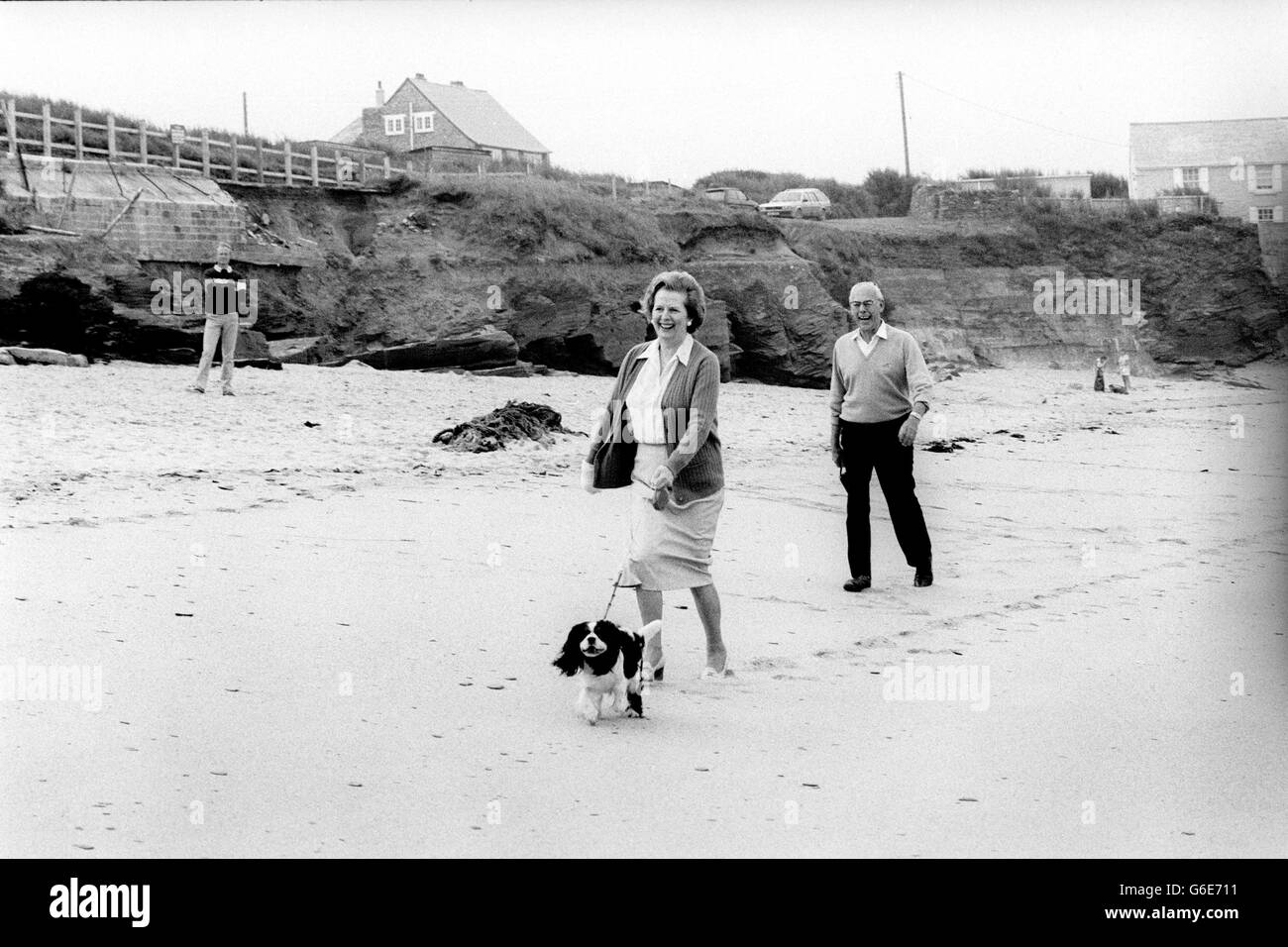 Le PM Margaret Thatcher et le mari Denis prennent leur hôte de vacances King Charles Spaniel pour une promenade le long de la plage à Constantine Bay, Cornwall. Banque D'Images