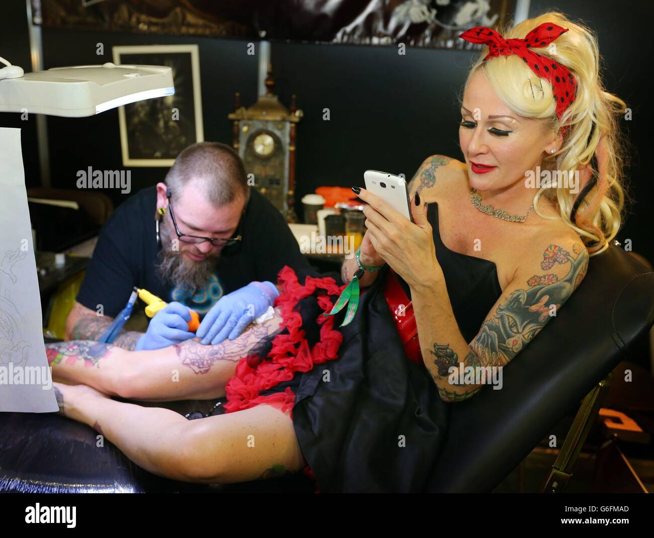 Une femme (nom non donné) vérifie son téléphone comme l'artiste de tatouage Mark Poole travaille sur sa jambe pendant le Tattoo Jam à Doncaster Racecourse. Banque D'Images