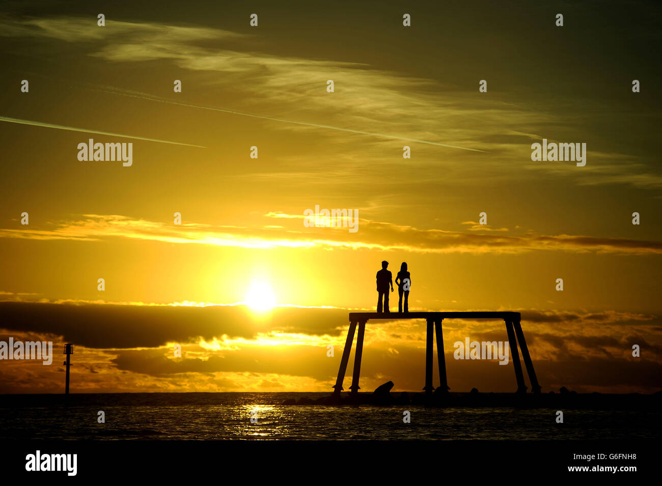 Le soleil se lève sur la sculpture 'COUPLE' de Sean Henry sur l'eau de rupture à Newbiggin-by-the-Sea, Northumberland. Banque D'Images