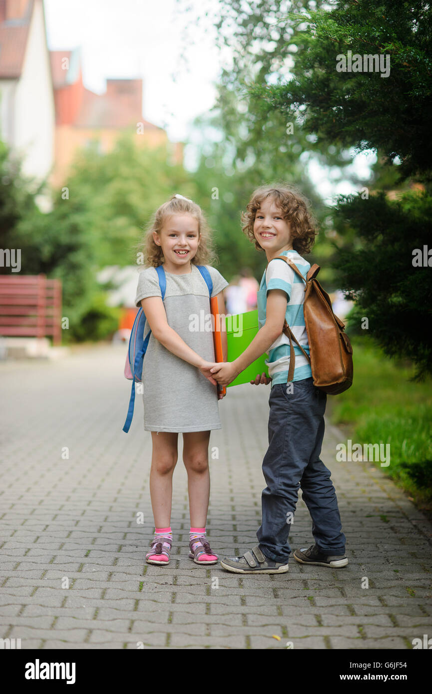 Garçon et fille avec des cartables tenir la main. Les enfants vont à l'école. Ils ont une bonne humeur. Chaude journée d'été. Les élèves de l'école avec un s Banque D'Images