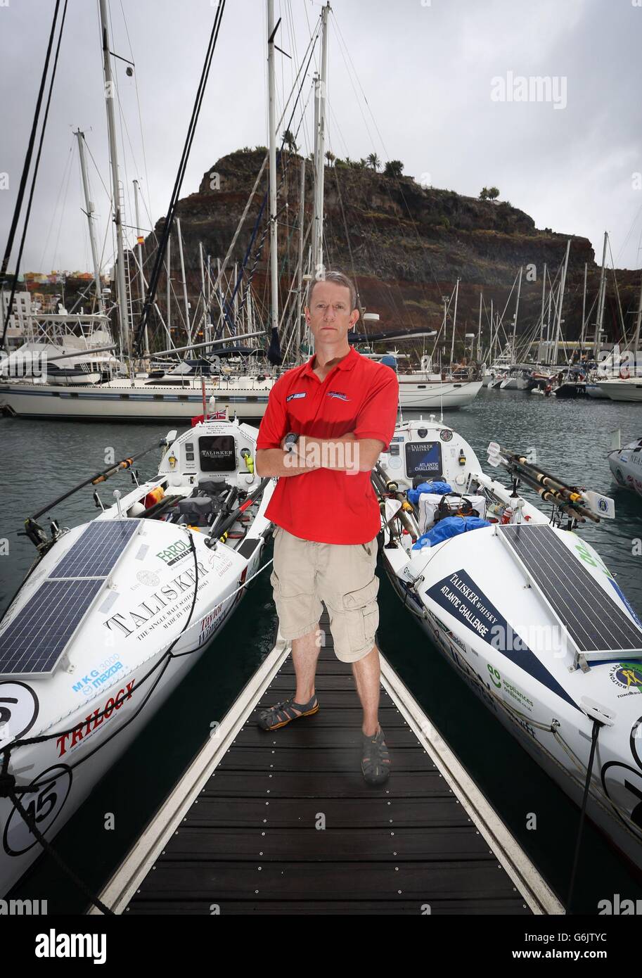 Ian Couch, officier de service et rameur expérimenté de l'Atlantique, pose avec deux bateaux à rames de l'Atlantique à Port San Sebastian, dans les îles Canaries, avant le début du défi atlantique Talisker Whiskey qui commence plus tard cette semaine. Banque D'Images