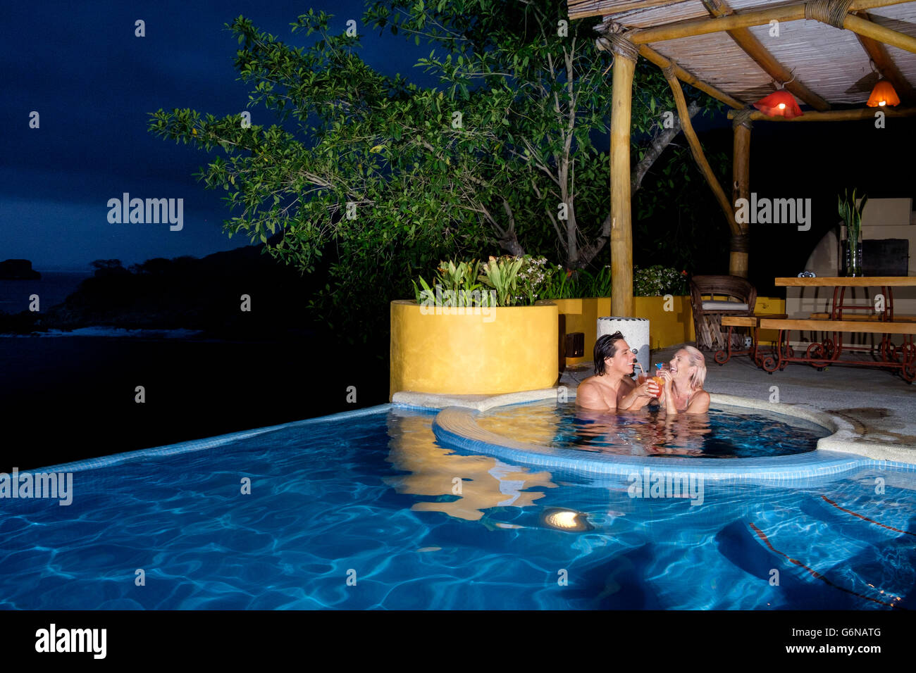 Couple enjoying cocktails dans la piscine de nuit Banque D'Images