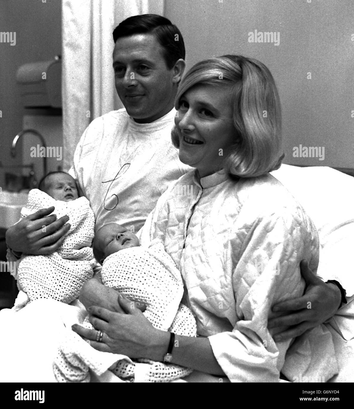 Michael Aspel, le lecteur de nouvelles de la BBC Television, porte un manteau médical blanc pour rendre visite à sa femme Ann et à leurs deux enfants, les jumeaux Jane (à droite) et Edward, à l'hôpital de la ville de Londres. Les bébés sont nés le 11 octobre. Banque D'Images