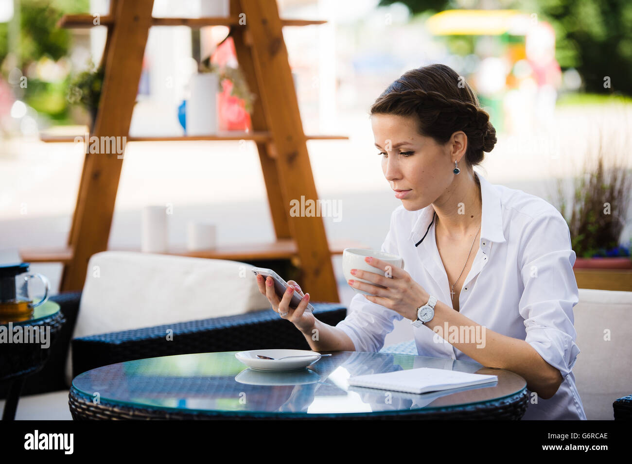 Portrait of young businesswoman à boire du café et à l'aide de téléphone mobile tout en restant assis sur le trottoir cafe Banque D'Images