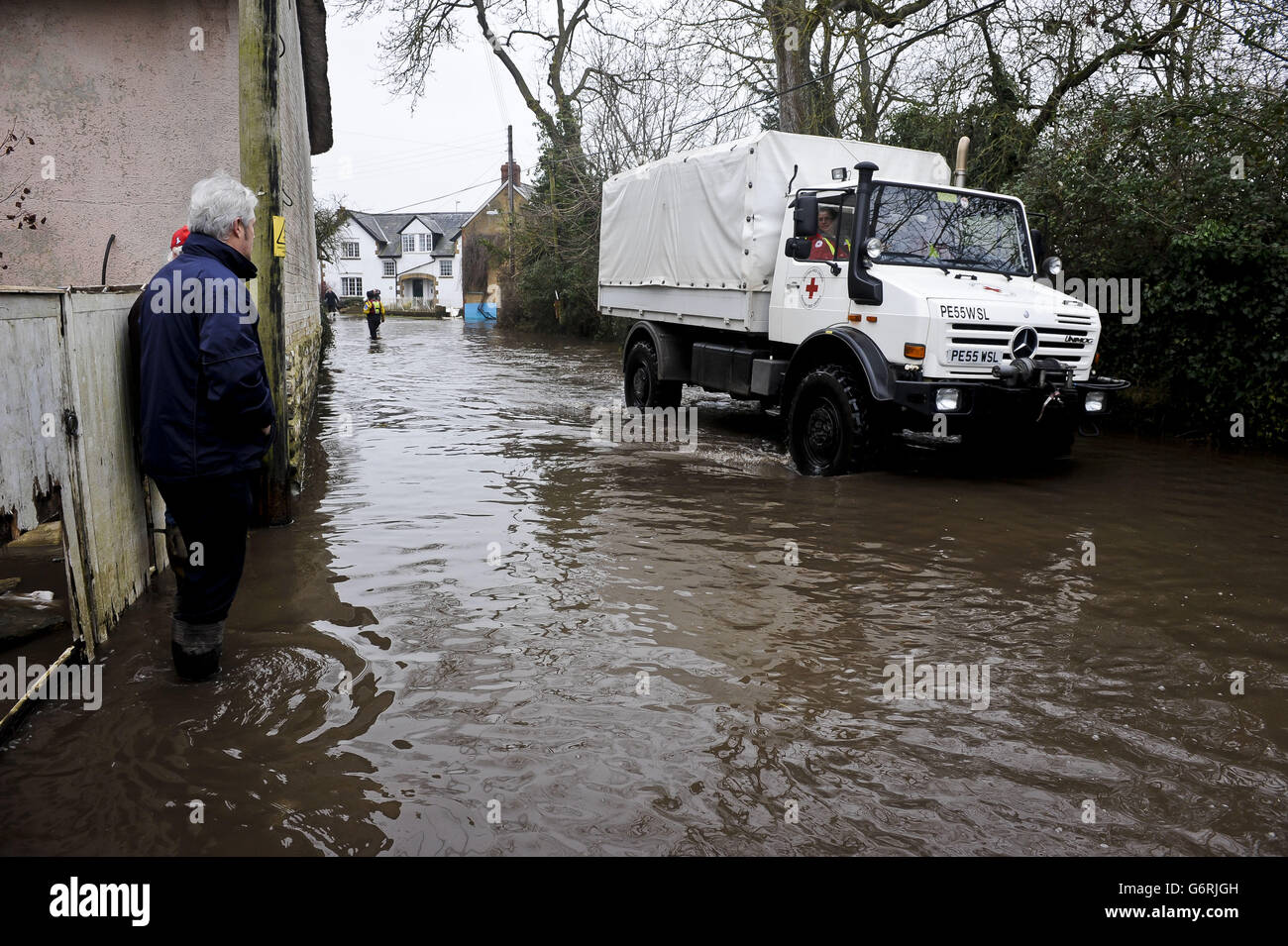 Un homme regarde un véhicule de la Croix-Rouge conduit une route inondée dans le village de Muchelney dans le Somerset. Banque D'Images