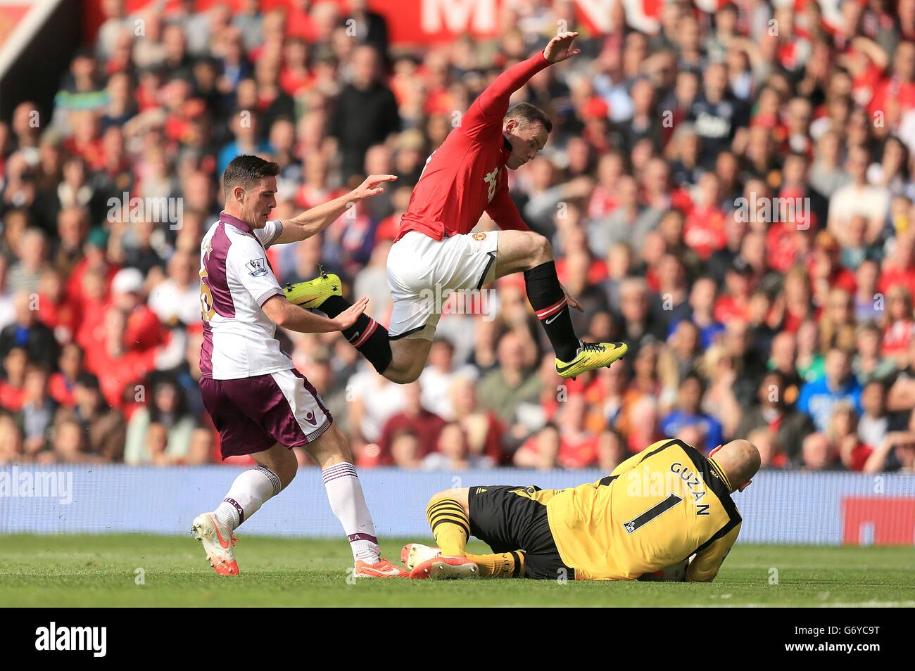 Wayne Rooney (au centre) de Manchester United haies un défi lancé par le gardien de but Brad Guzan (au sol) d'Aston Villa qui a revendiqué le ballon Banque D'Images