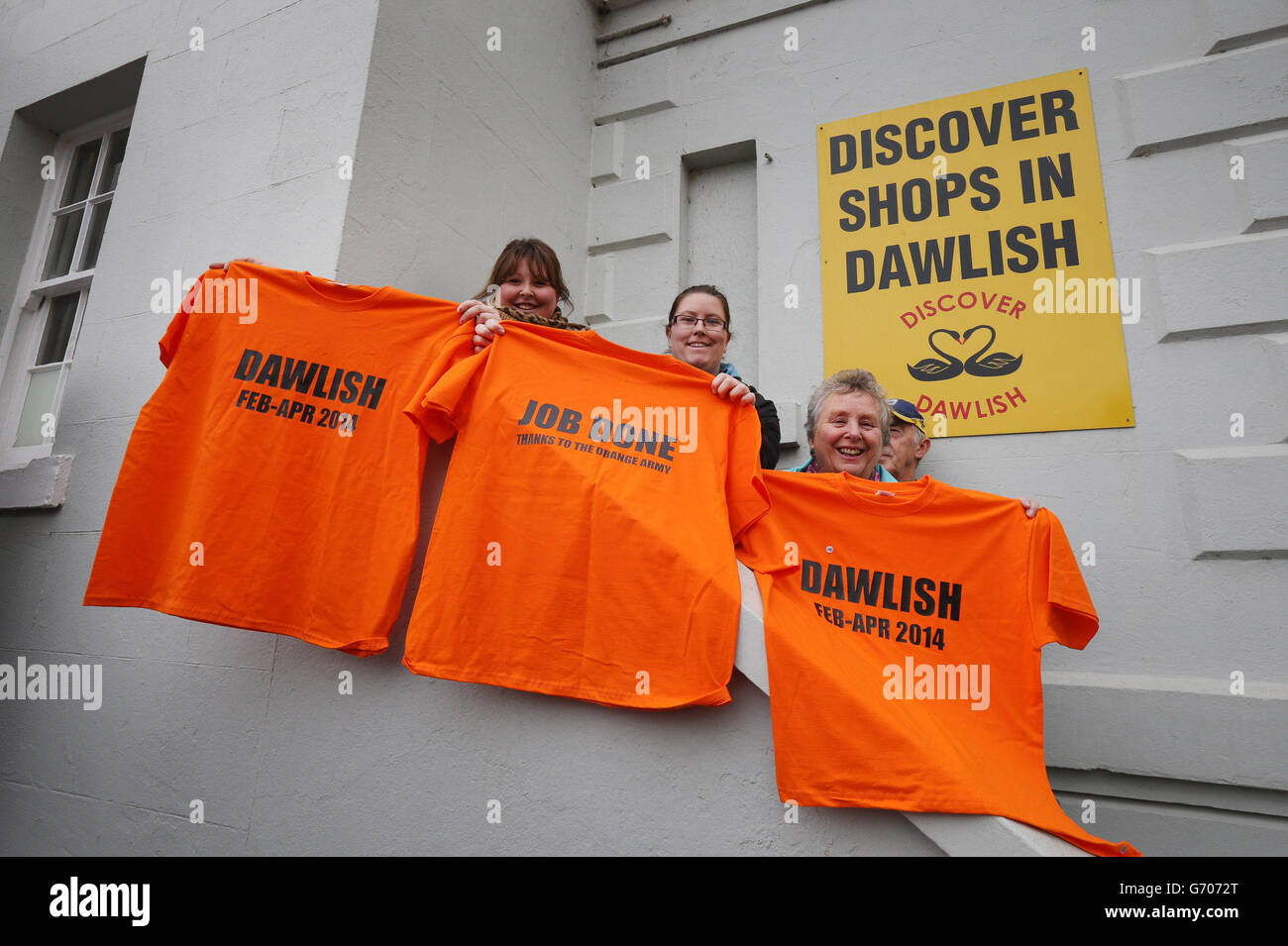 Les habitants de la région tiennent des tee-shirts disant « Job done Thanks to the Orange Army » et « awlish Feb-April 2014 » à la gare de Dawlish, Devon, lors d'une visite du Premier ministre David Cameron, après la réouverture de la ligne de chemin de fer bâtue par la tempête. Banque D'Images