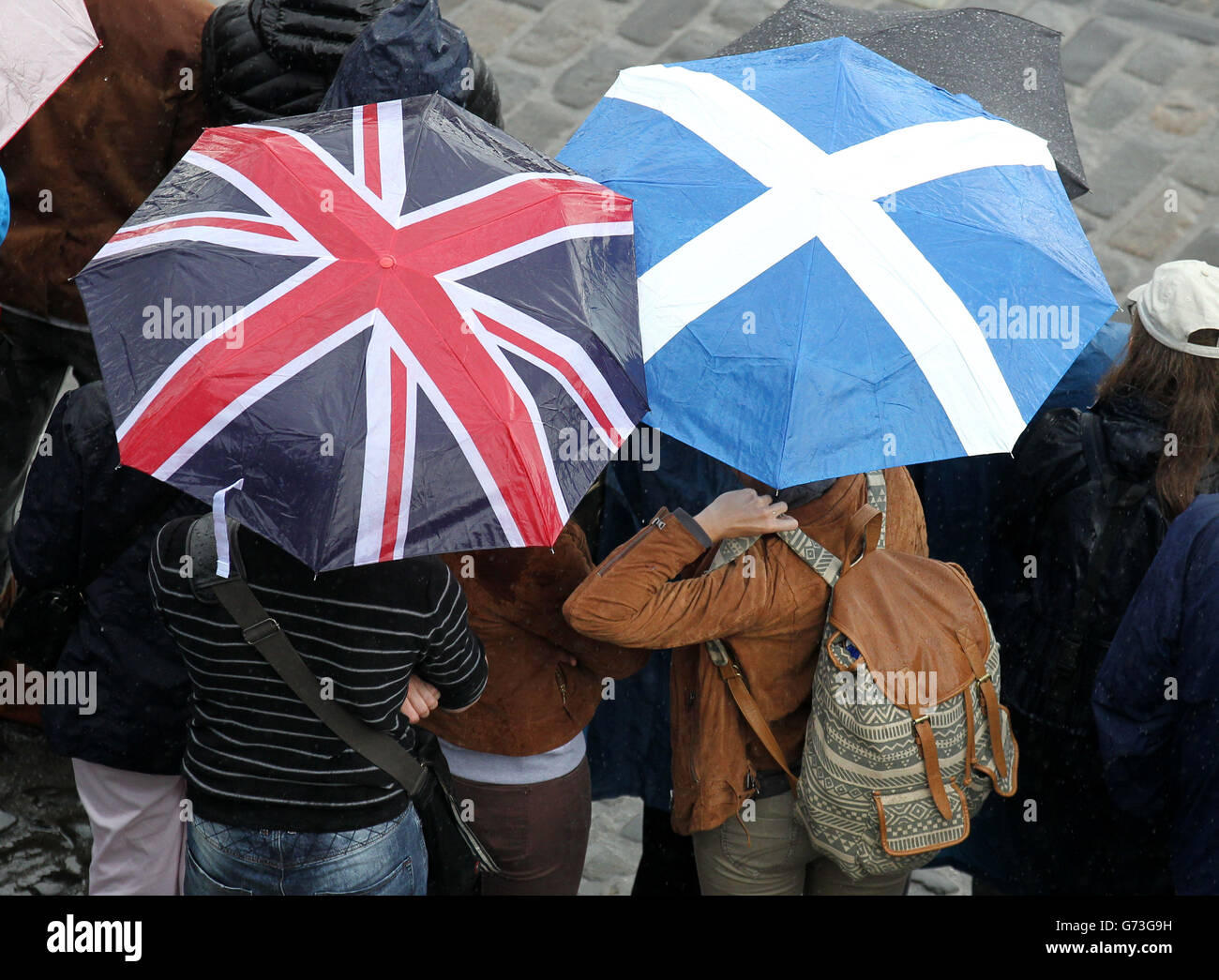 Les gens se réfugient sous un saltire et un parapluie Union Jack pendant qu'ils regardent les cadets de l'officier du corps d'entraînement des universités de la ville d'Édimbourg déclencher une Salute royale de 21 canons au château d'Édimbourg pour marquer le 93e anniversaire du duc d'Édimbourg. Banque D'Images