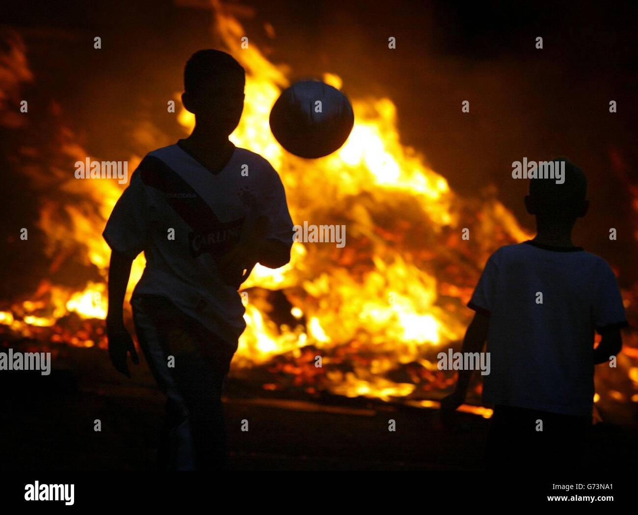 Les enfants jouent au football dans l'un des nombreux feux de joie qui s'incendient à Belfast et dans le reste de l'Irlande du Nord à la veille de la plus grande journée de marche du calendrier de l'ordre d'Orange.Le 12 juillet, des dizaines de milliers d'Orangemen et de groupes défilent à travers la province pour célébrer la victoire du roi Guillaume d'Orange sur le roi catholique James, à la bataille de la Boyne en 1690. Banque D'Images