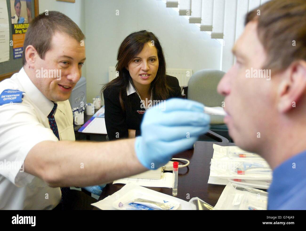 (De gauche à droite) Chris Chives, agent de détention de la police du Grand Manchester, est surveillé par Caroline Flint, ministre de l'intérieur, le mardi 27 juillet 2004, alors qu'il effectue un test de dépistage de drogues sur un homme. Les tests de dépistage de la drogue chez les enfants délinquants dès 14 ans doivent commencer dans quelques jours, ont annoncé aujourd'hui les ministres. La ministre du Home Office, Caroline Flint, a lancé un programme dans 10 zones pilotes en Angleterre. Le dépistage de drogues chez les adultes suspects a été introduit en octobre 2001, mais lorsque le nouveau pilote sera lancé samedi, ce sera la première fois que l'initiative sera étendue aux enfants. Banque D'Images