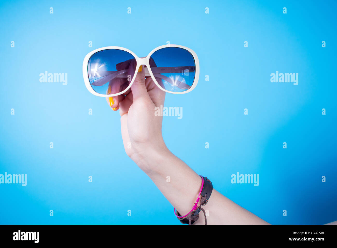Woman holding big sunglasses contre fond bleu Banque D'Images