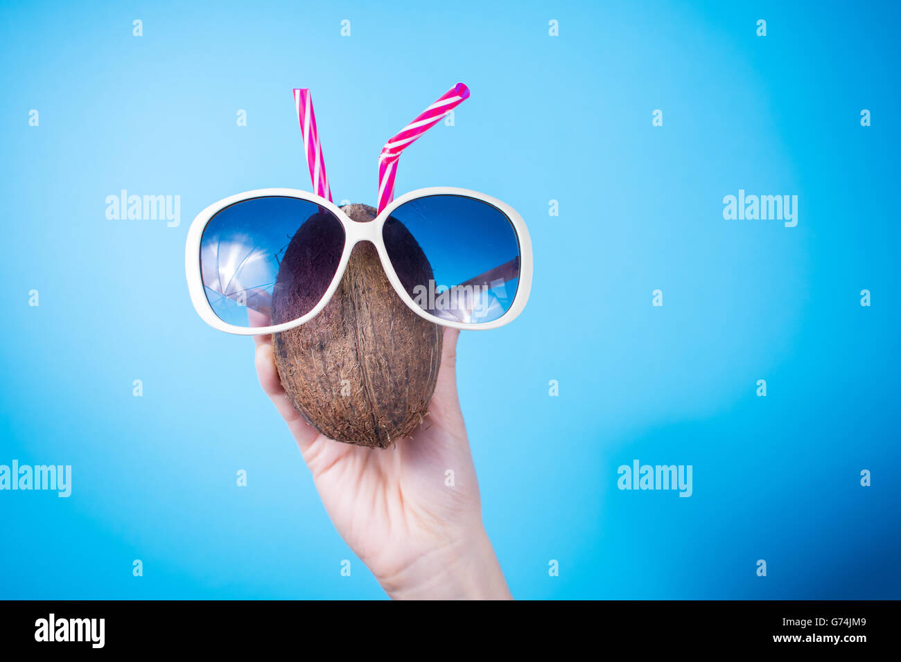 Femme main tenant une noix de coco et des lunettes contre fond bleu Banque D'Images